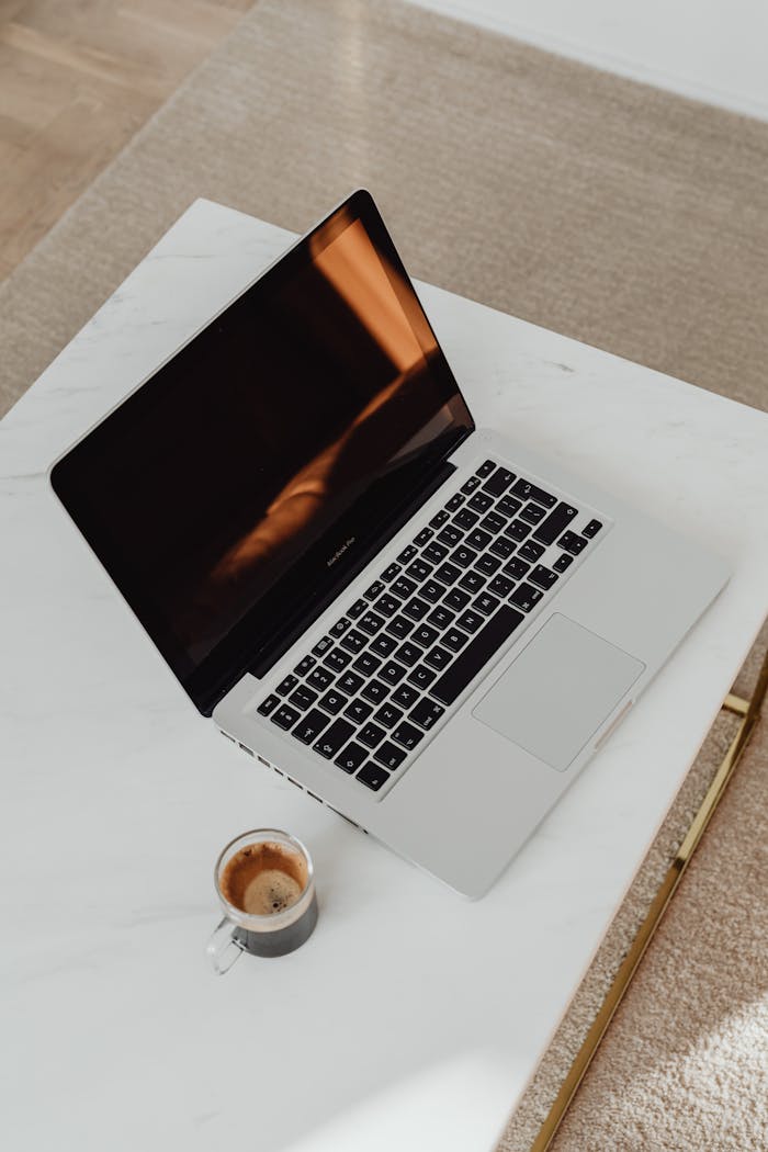 A top view of a laptop and a cup of coffee on a white table, evoking productivity.